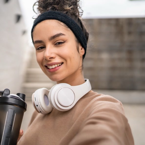 A woman with a nutrition shaker and headphones, ready to move
